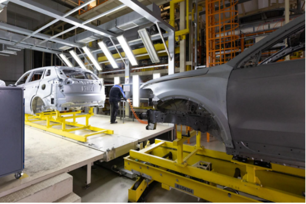 A worker supervises as cars get assembled in a manufacturing plant