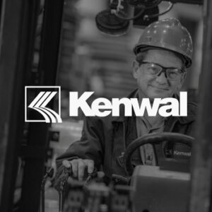 A black and white photograph of a smiling Kenwal worker wearing a hard hat and safety glasses while operating machinery. Embedded in the center is a white version of the Kenwal logo.