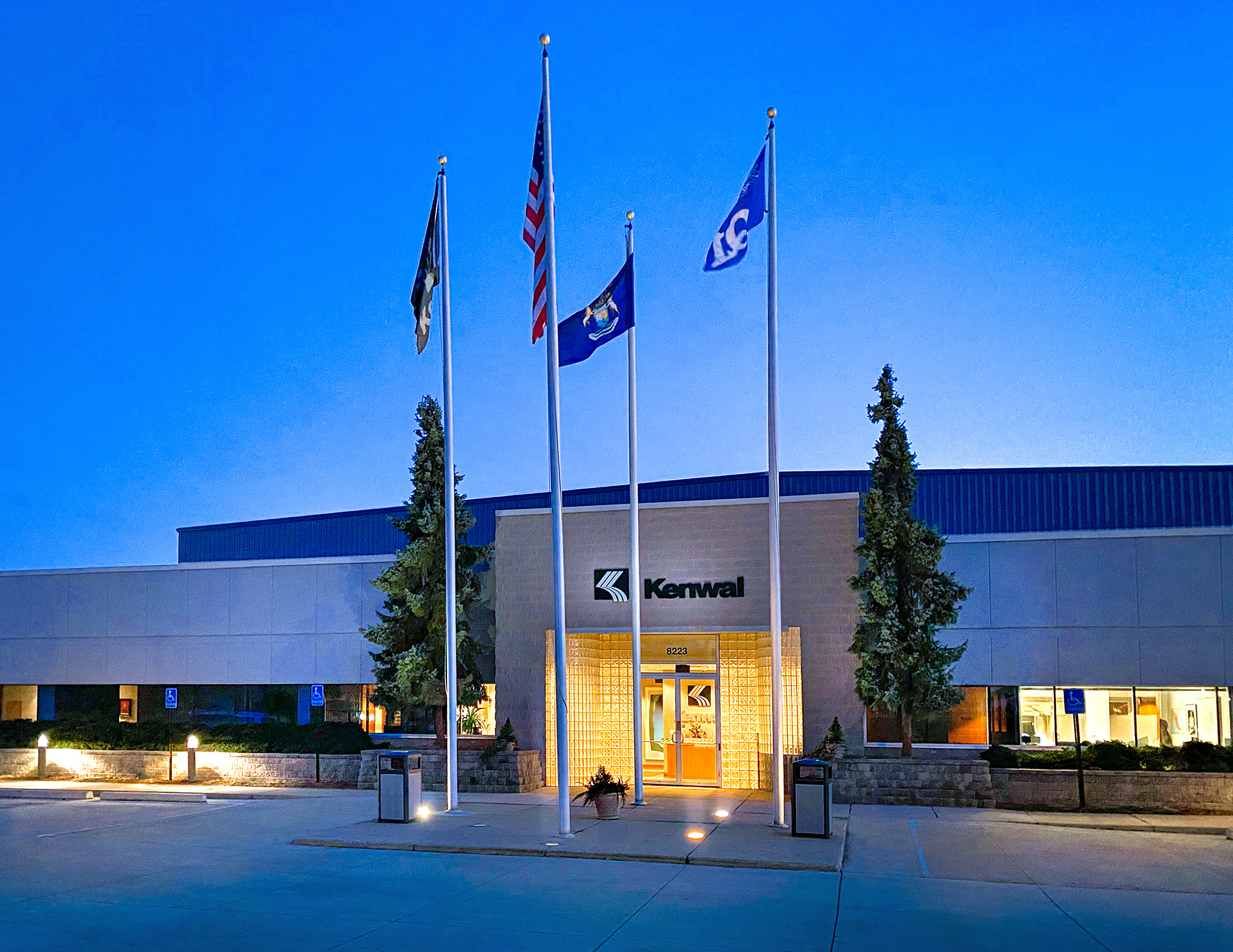 Kenwal's Dearborn headquarter's building, interior lights on and 4 flags standing in front of entrance