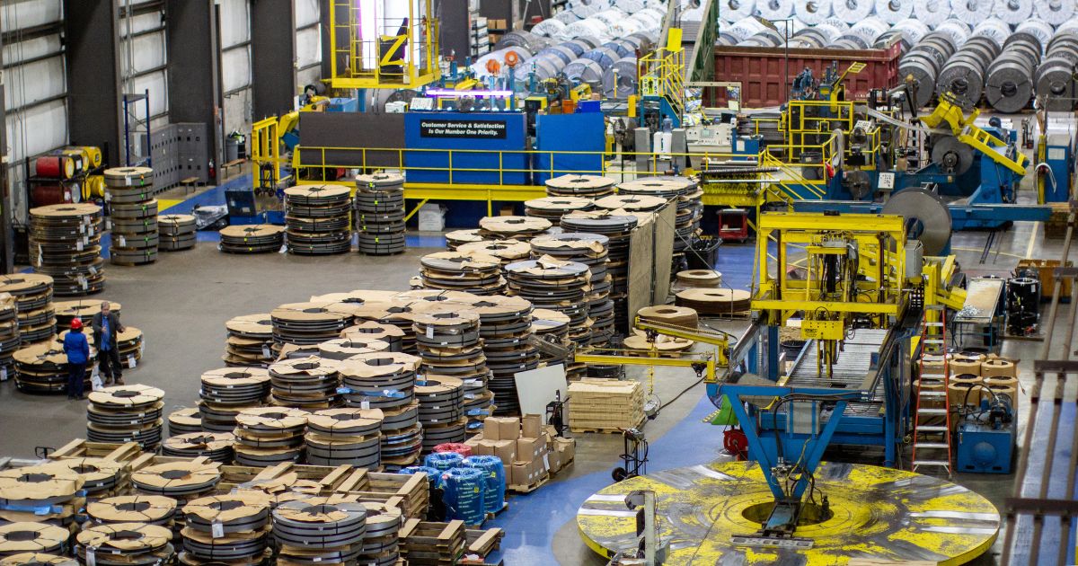 The interior of Kenwal’s manufacturing facility in Tennessee where a yellow overhead crane operates above extensive stacks of steel coils and heavy processing equipment.