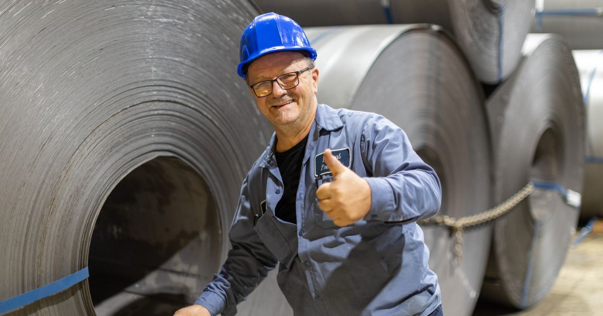 A steel expert smiling and giving a thumbs up while inspecting high-quality, flat-rolled steel coils manufactured by trusted parter, Kenwal Steel.
